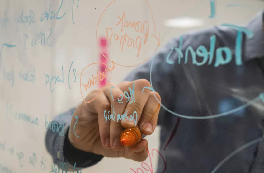 Someone writing on a glass board with a whiteboard marker.