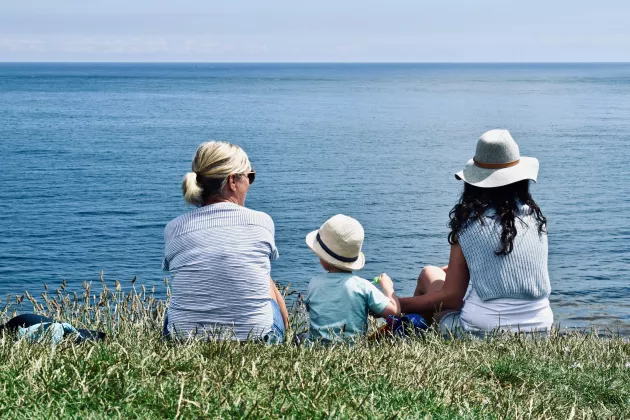 Tre generationer sitter i gräset och tittar mot havet.