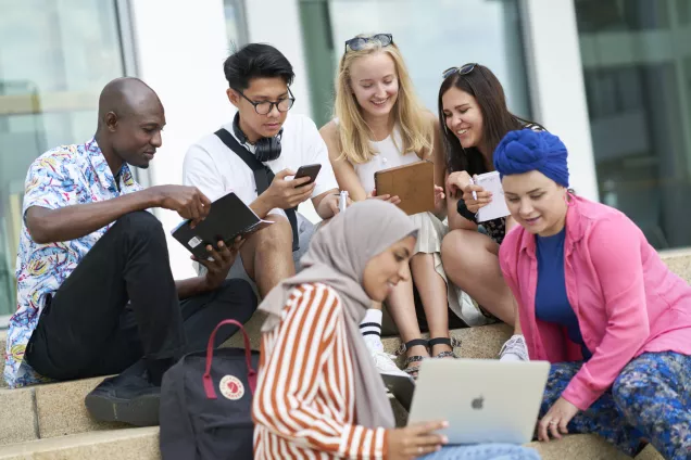 Många studenter samlade utomhus kring en laptop. Foto. 